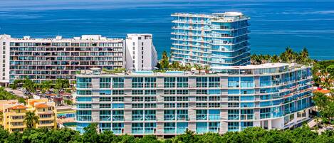 A multi-story hotel with a curved facade, large windows, and a view of the ocean.