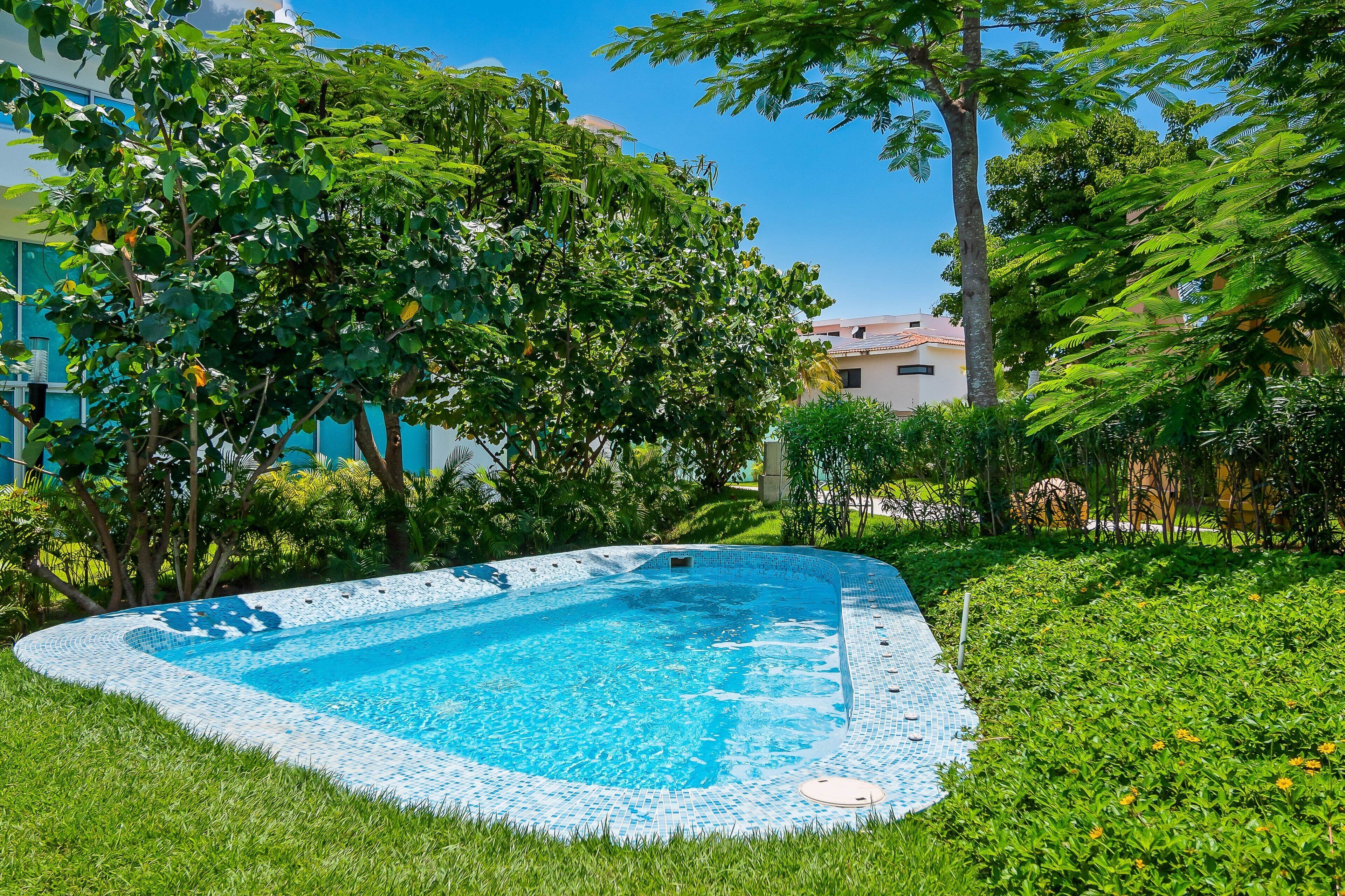 Une piscine entourée d’une végétation luxuriante, avec un bâtiment en arrière-plan.