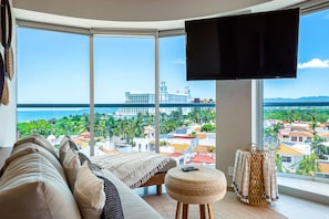 Ein modernes Wohnzimmer mit großem Fenster, Flachbildfernseher, Sofa und kleinem Hocker.