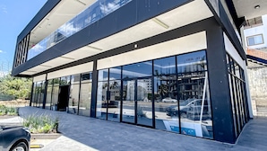 A modern building with large glass windows, a flat roof, and a visible entrance. - Ocean-view Condo With Infinity Pool, Rooftop Lounge, & Private Balcony (Bucerías)