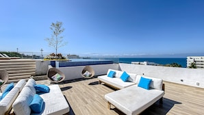 A rooftop terrace with a pool, white sofas with blue cushions, and a view of the sea. - Ocean-view Condo With Infinity Pool, Rooftop Lounge, & Private Balcony (Bucerías)