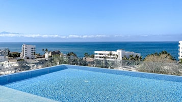 Una piscina azul cristalina con vista al océano y edificios al fondo.