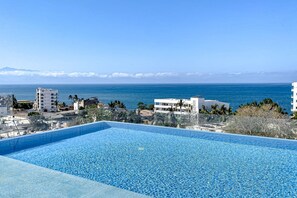 A clear blue swimming pool with a view of the ocean and buildings in the background. - Ocean-view Condo With Infinity Pool, Rooftop Lounge, & Private Balcony (Bucerías)