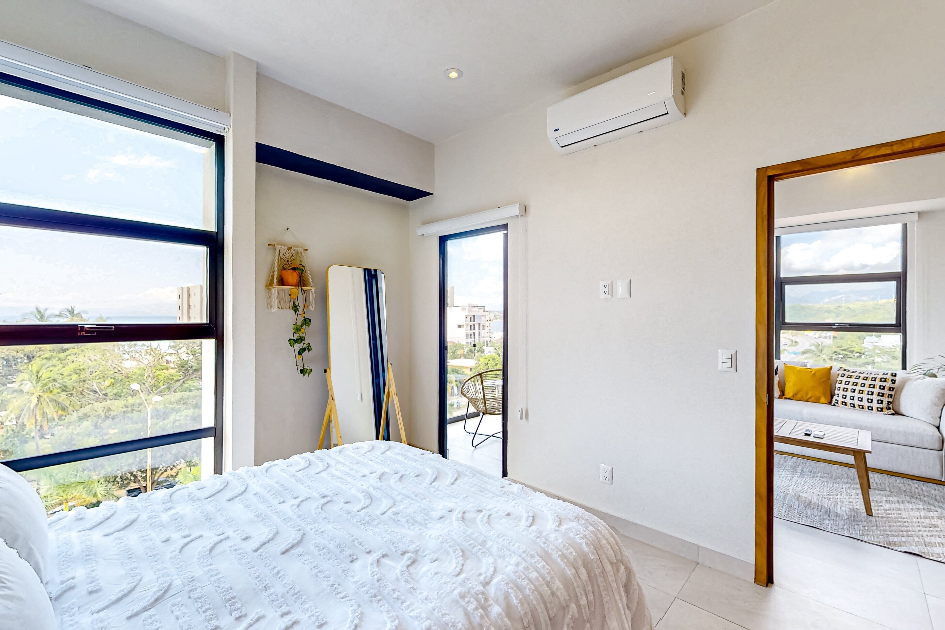Une chambre avec un grand lit, un balcon avec un canapé et une vue sur la verdure.