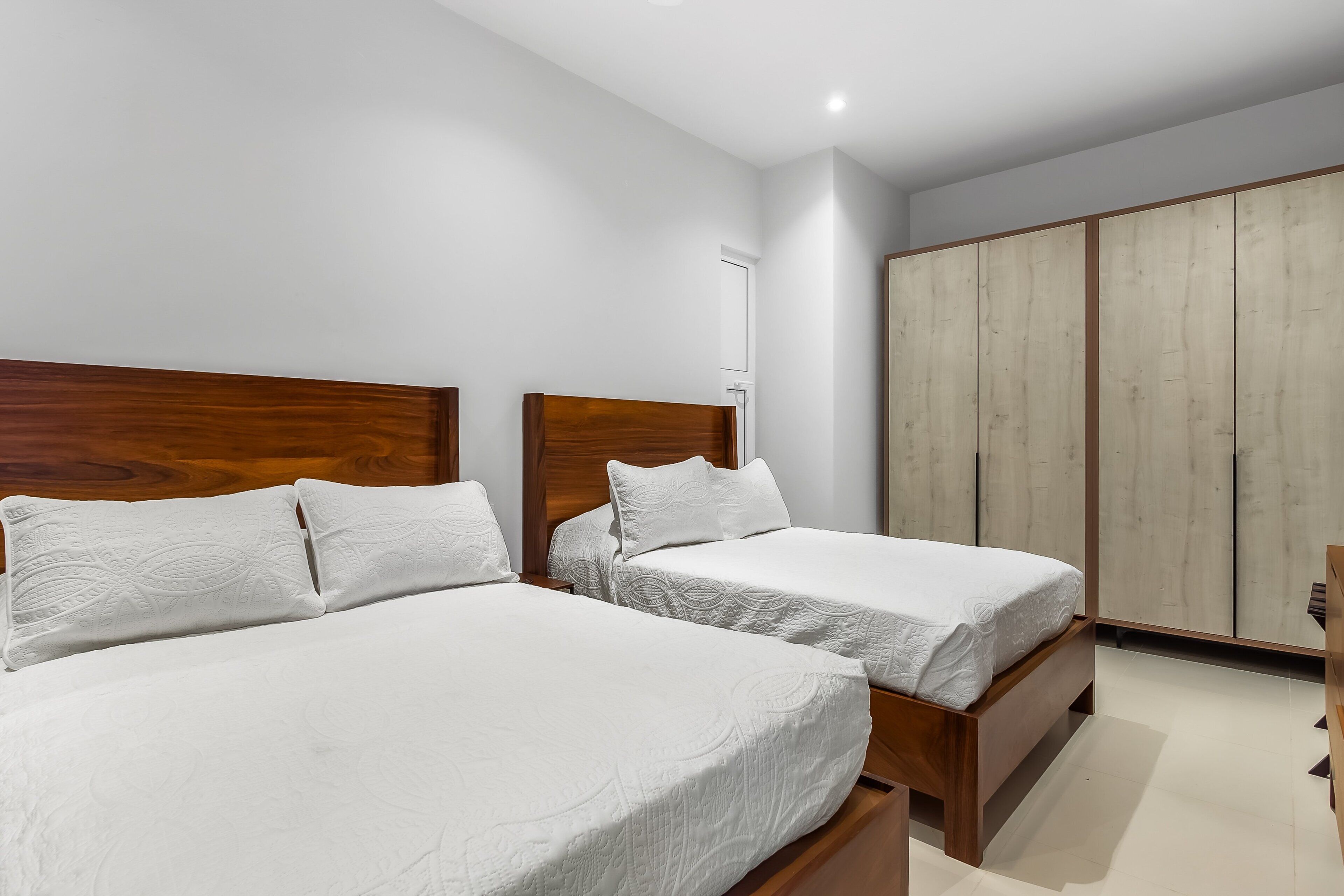 A bedroom with two beds, wooden headboards, a wardrobe, and a small bedside table.