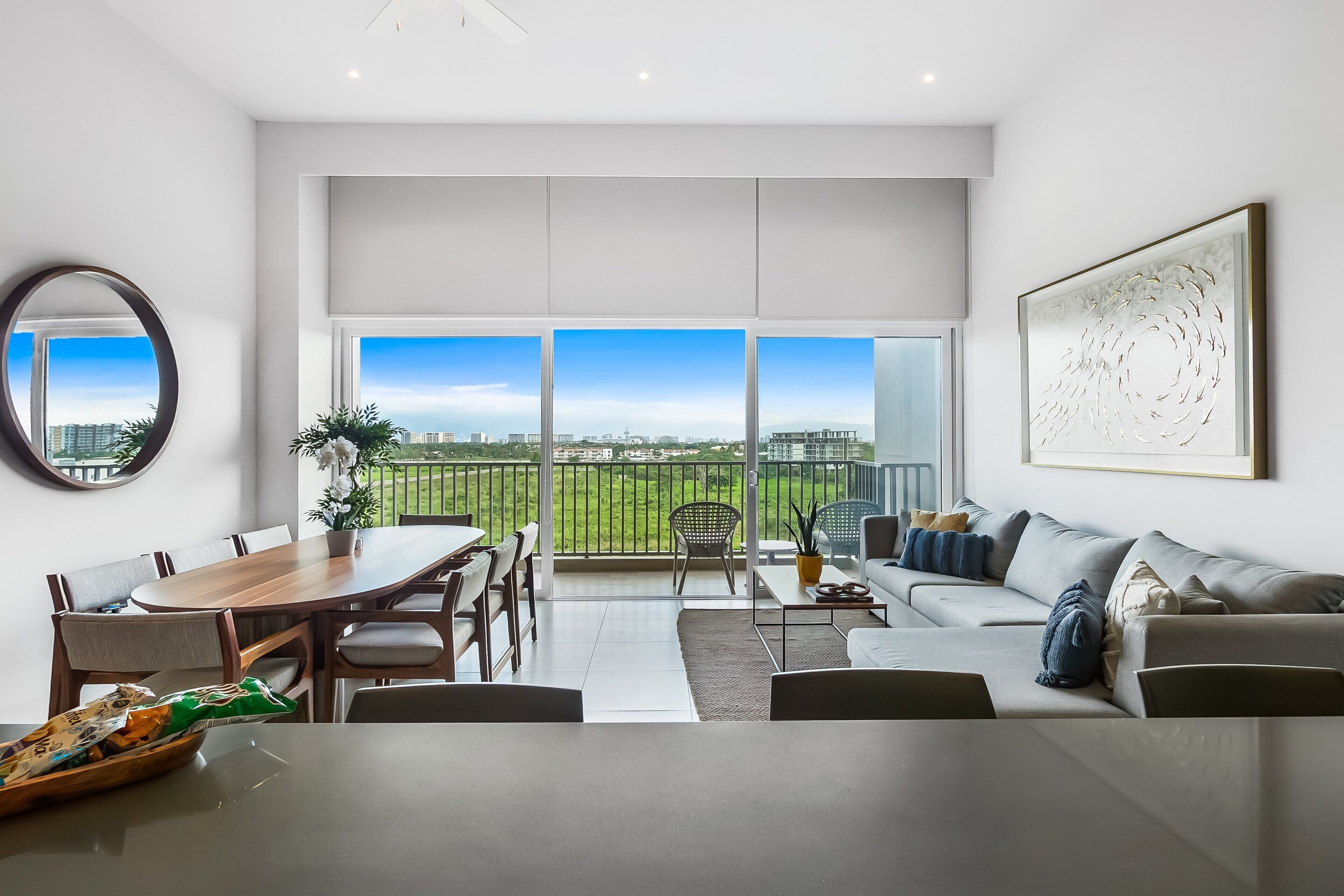 Un salon moderne avec un coin repas, de grandes fenêtres, un balcon et une vue sur la ville.