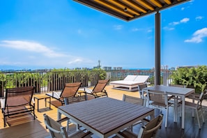 Una terraza al aire libre con muebles de madera, una silla lounge blanca y vistas a un horizonte urbano.