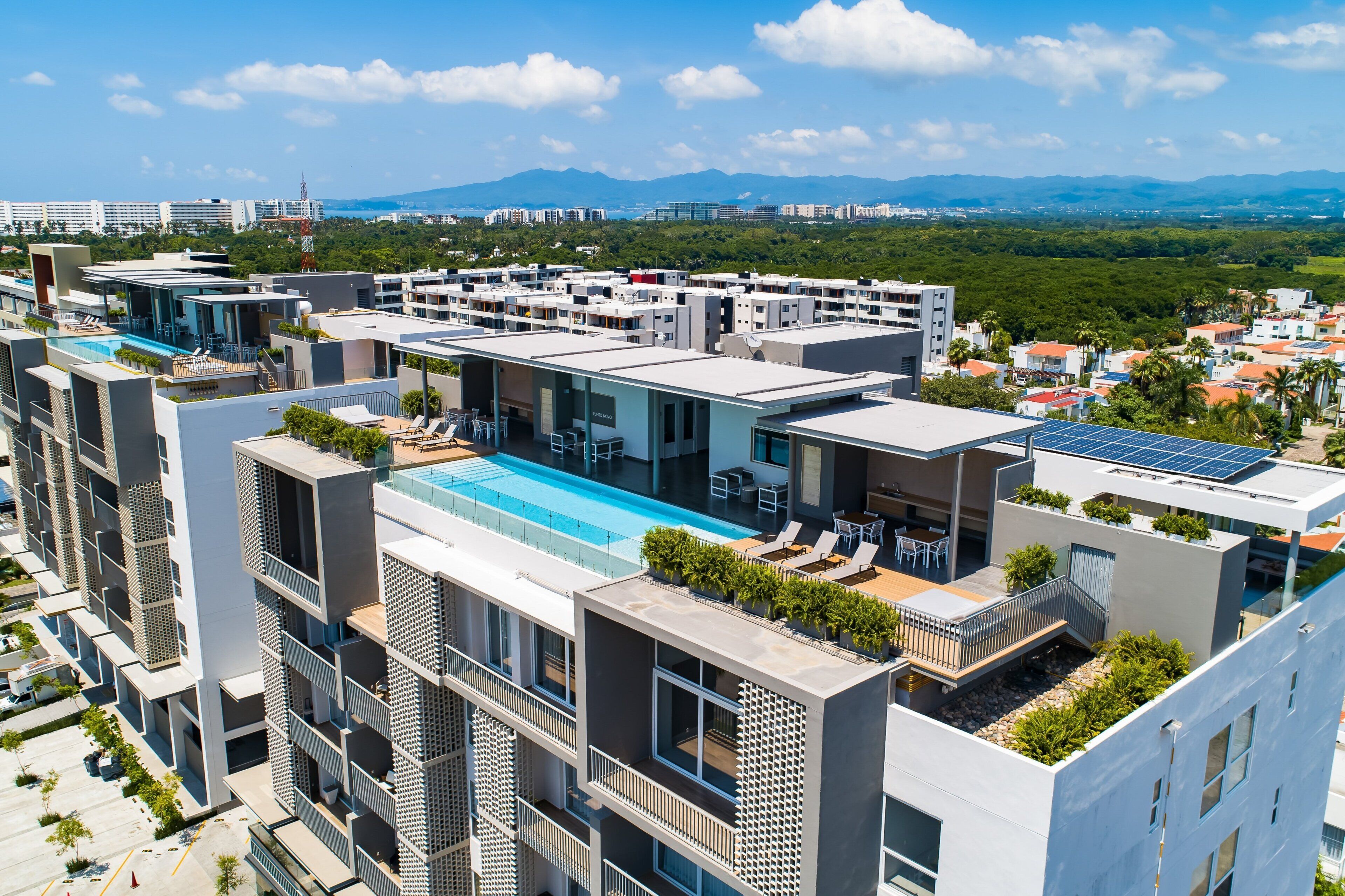 Un moderno edificio de varios pisos con piscina en la azotea, balcones y paneles solares.