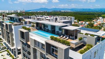 Un moderno edificio de varios pisos con piscina en la azotea, balcones y paneles solares.