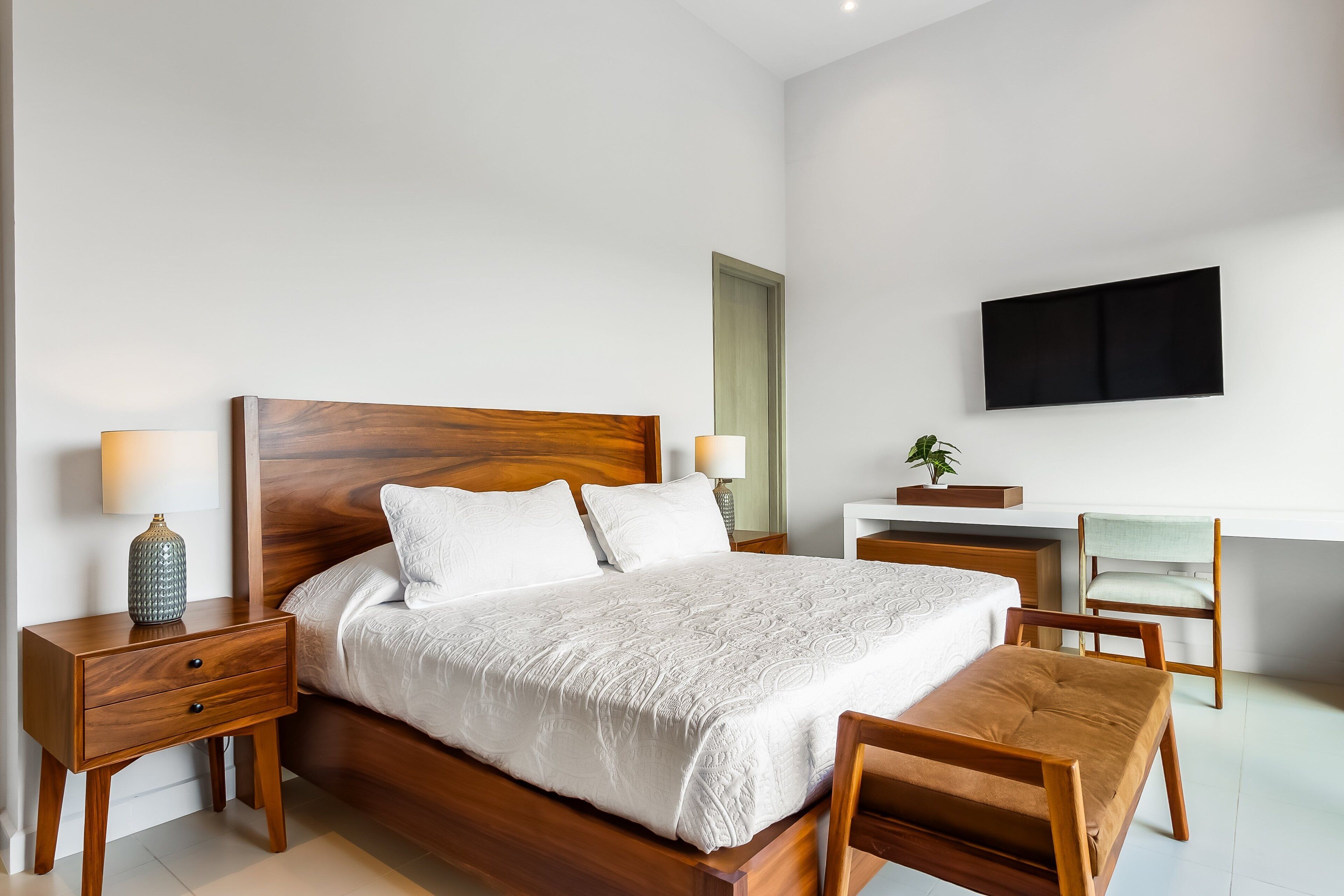 A modern bedroom with a wooden bed, bedside tables, a desk, and a flat-screen TV.
