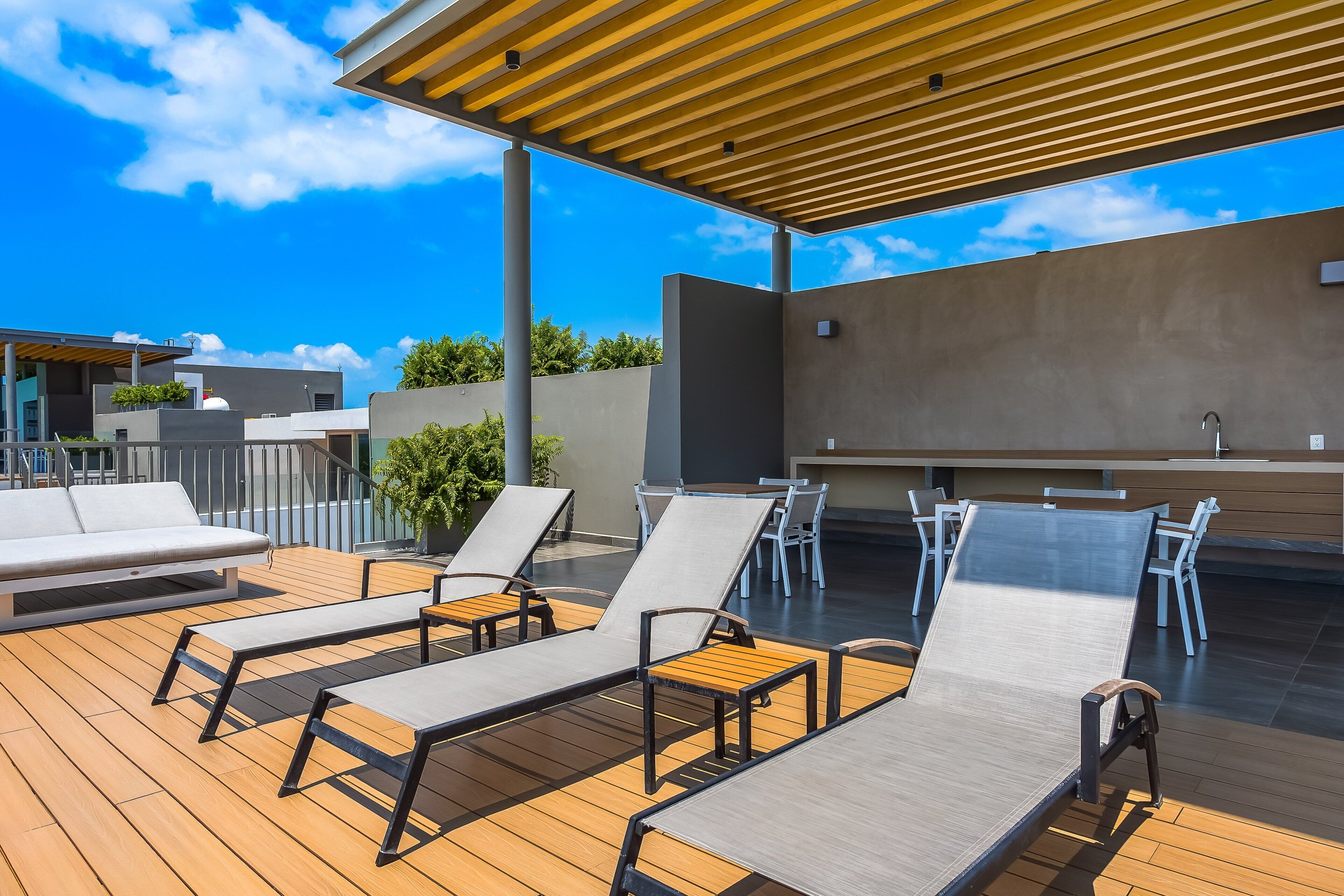 A rooftop deck with lounge chairs, a table, and a grill area.