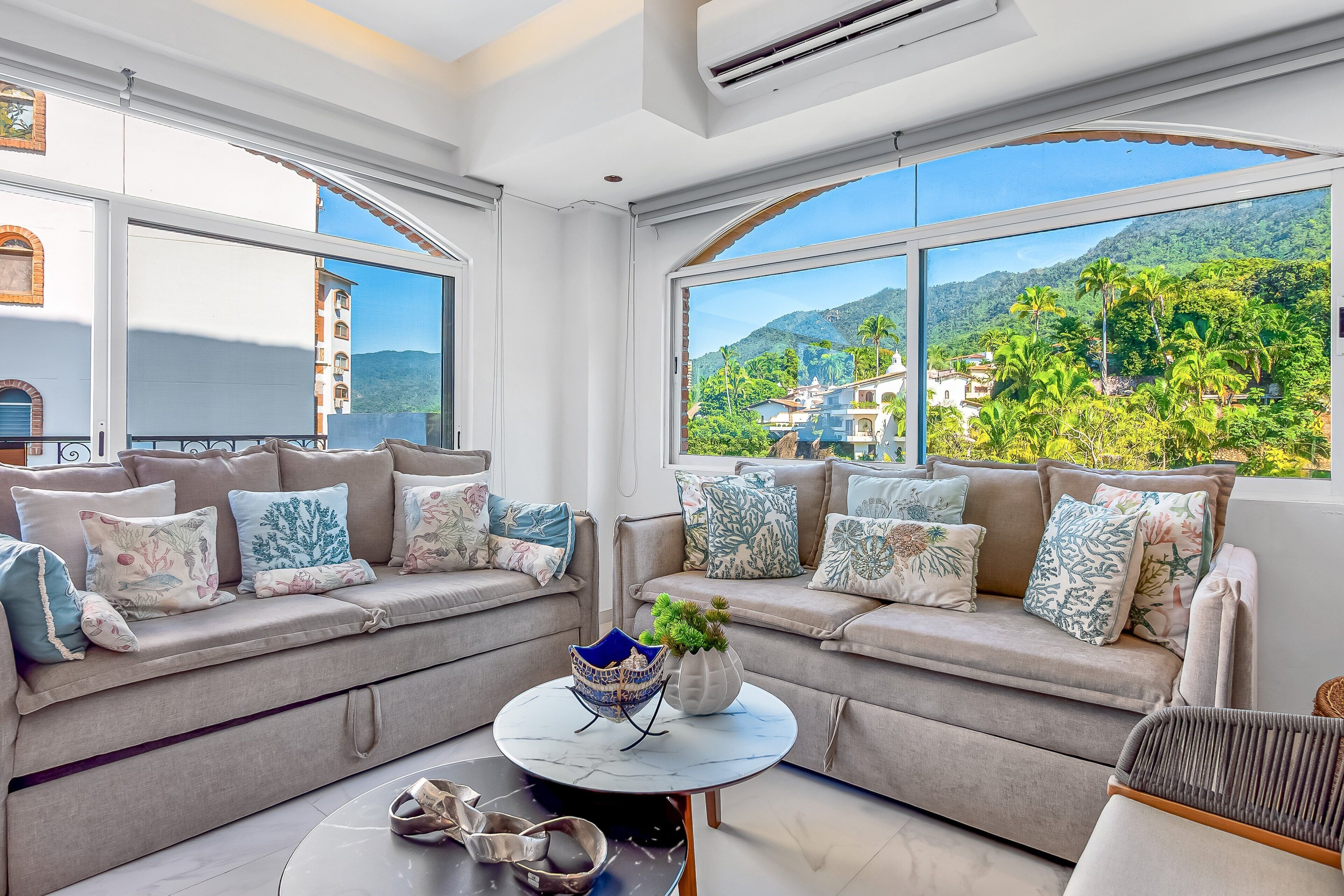 A modern living room with a sofa set, a round coffee table, and a view of a mountainous landscape.