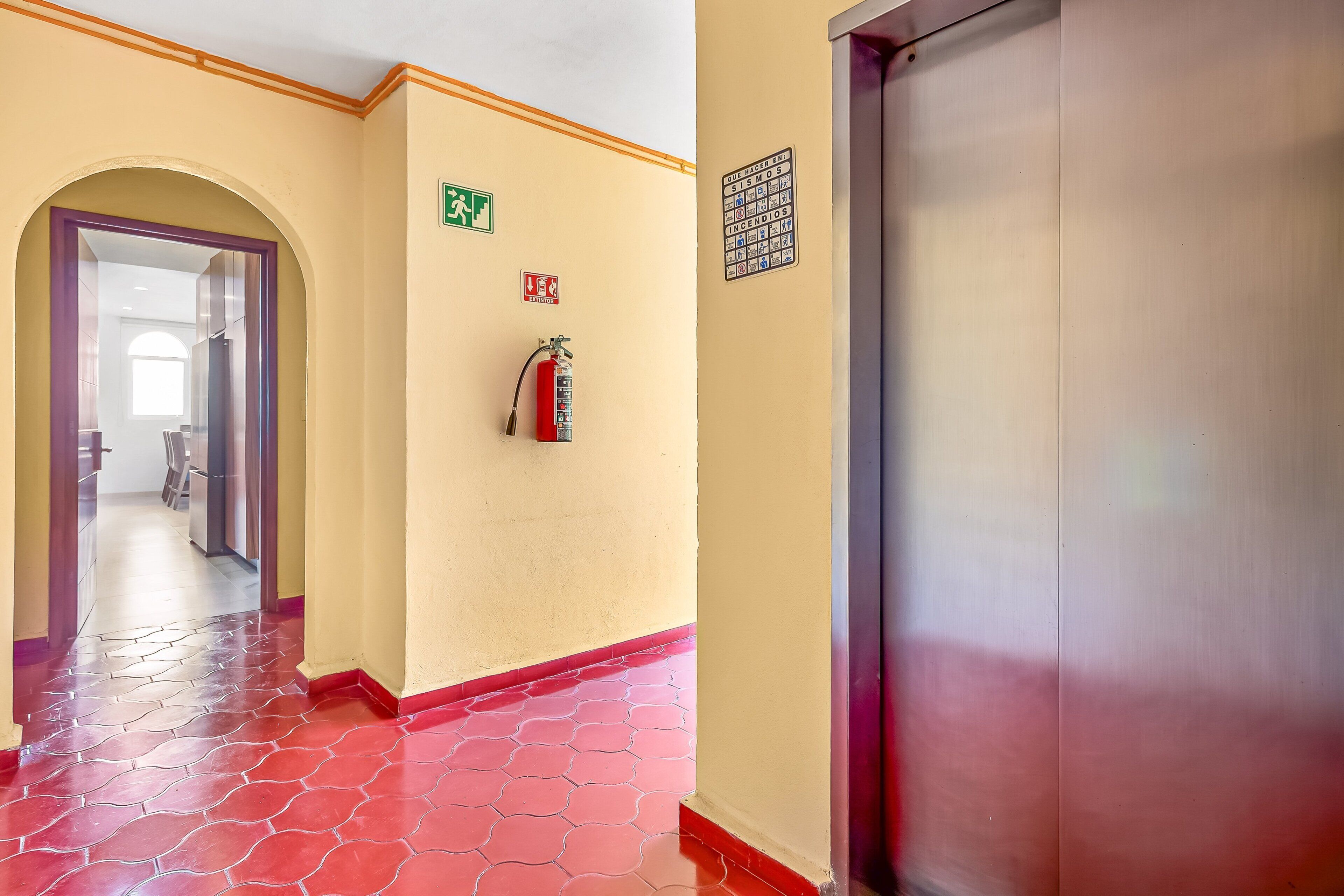 A hallway with a fire extinguisher, exit signs, and a door.