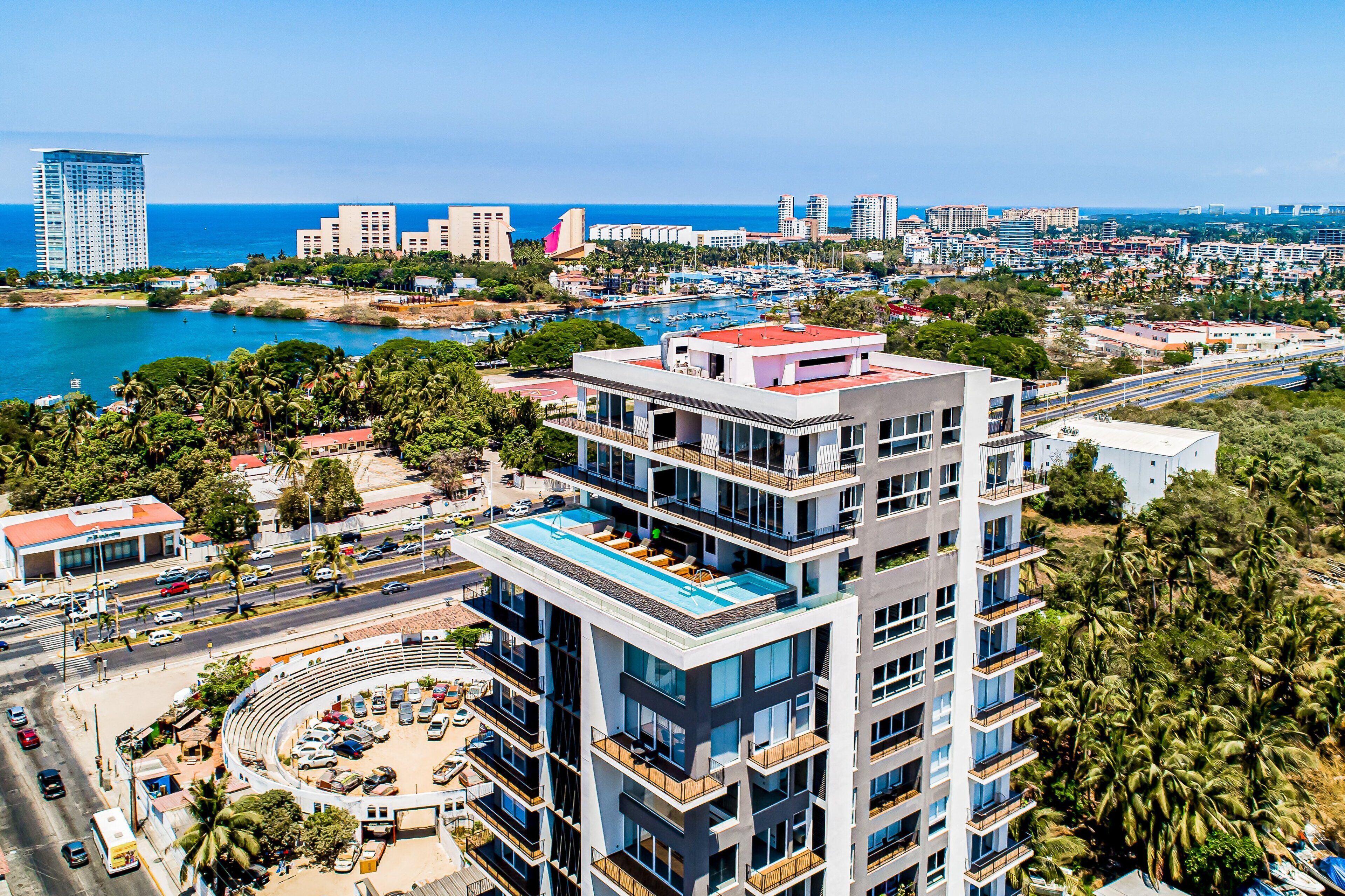 A high-rise hotel with multiple balconies, a rooftop pool, and a view of the surrounding cityscape and coastline.
