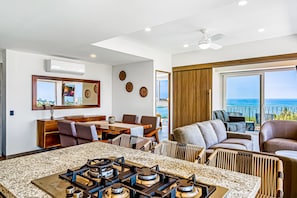 A modern kitchen with a gas stove, dining area with chairs, and a large window overlooking the sea. - Ocean-view Condo in Puerto Vallarta With Rooftop Pool, Fitness Room, and Balcony (Puerto Vallarta)