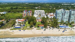 Un hotel sul lungomare con diversi edifici, una spiaggia e palme.