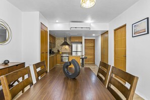 A dining area with a wooden table and chairs, a unique black circular object on the table, and a kitchen in the background. - Stylish Beach Condo With Private Balcony, Pool, AC and Fitness Room (Nuevo Nayarit)