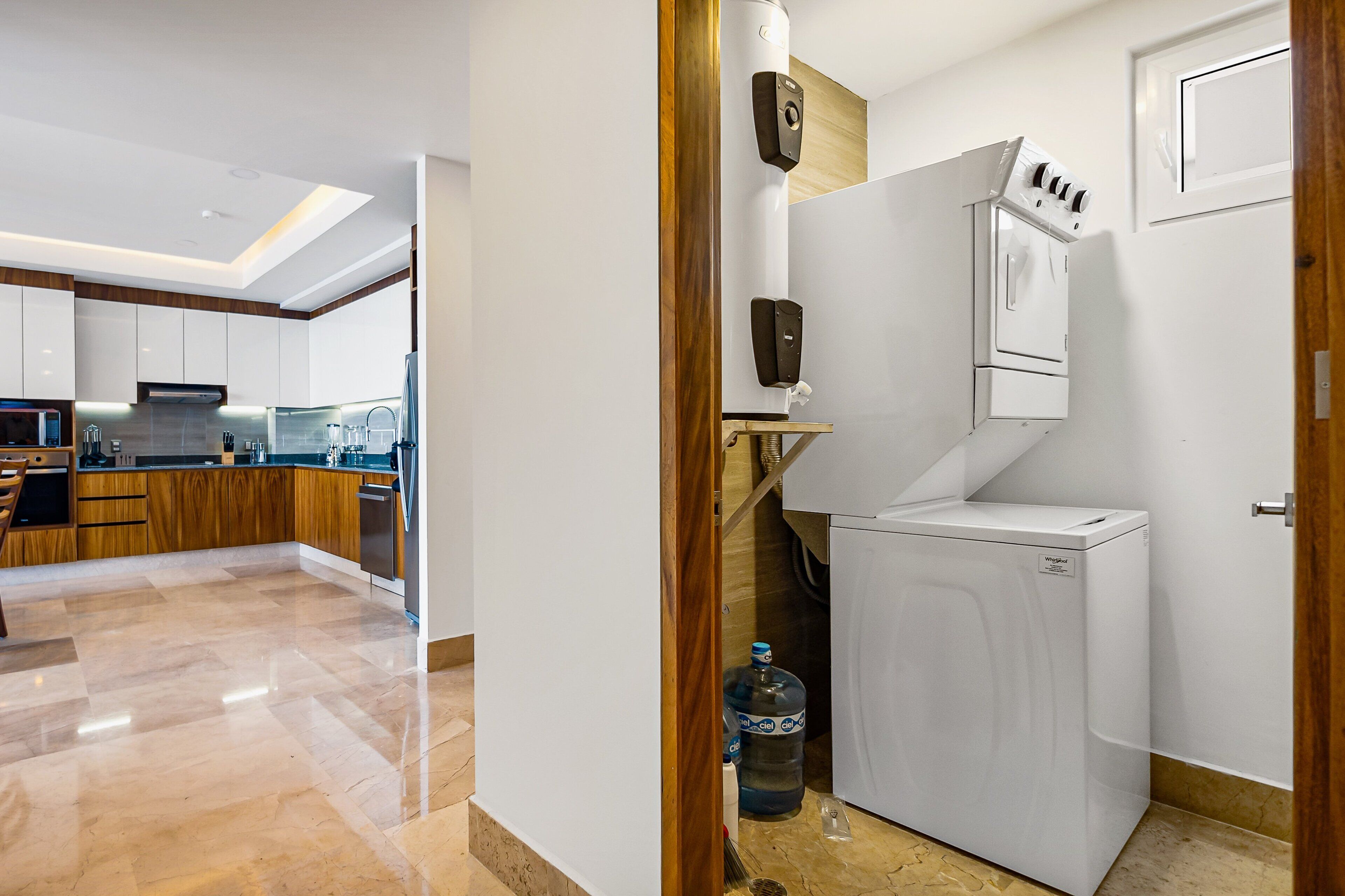 A modern kitchen with a built-in washer and dryer, a large water dispenser, and a wooden cabinet.