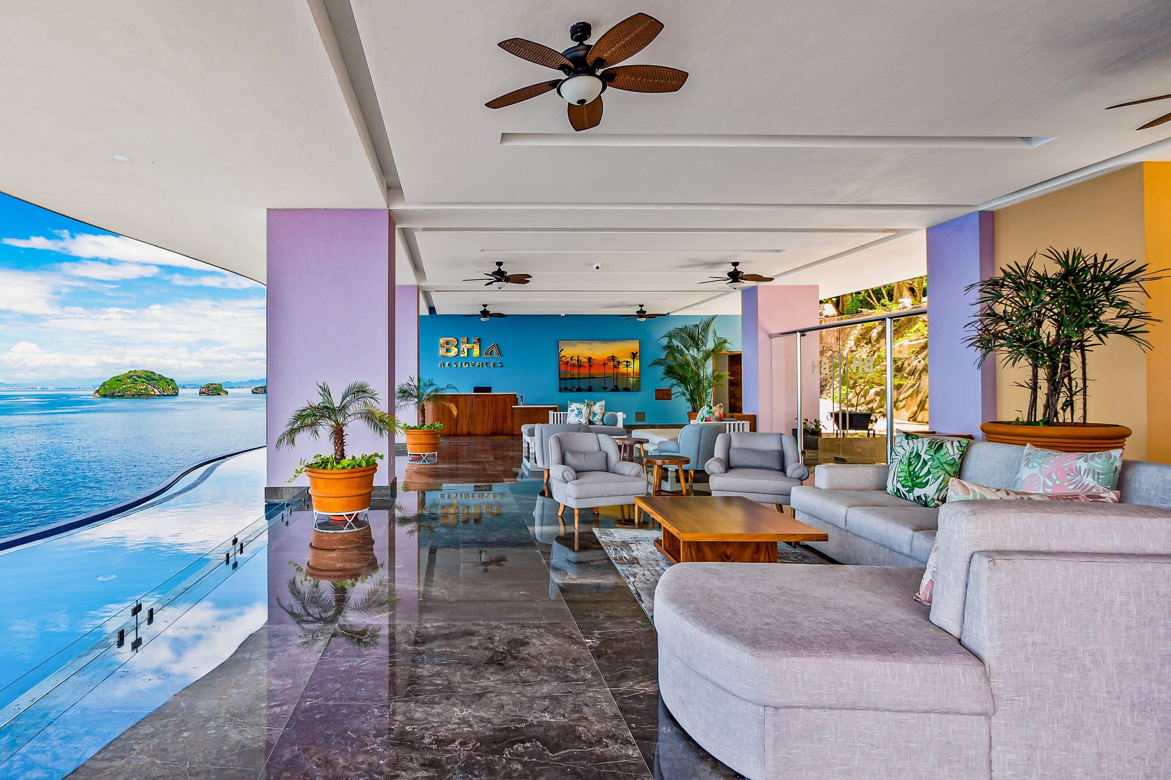 A modern hotel lobby with a pool, seating area, and a view of the sea.