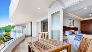 A balcony with a wooden table and chairs, a bed with blue and white bedding, and a view of the sea. - Luxurious Condo With Huge, Oceanfront Balcony, Pool & Pool spa (Puerto Vallarta)