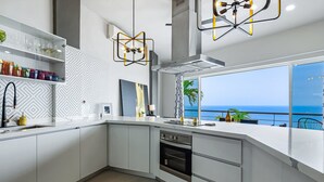 A modern kitchen with white cabinetry, a built-in oven, and a large window overlooking the sea. - Dog-friendly Ocean View Penthouse & Studio With a Full Kitchen & Kitchenette (Puerto Vallarta)