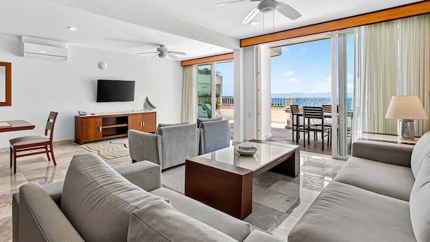 A modern hotel room with a balcony, a flat-screen TV, a sofa, a coffee table, and a dining area with a view of the ocean. - Modern Coastal Villa With Ocean Views, Pool, Wifi & Full Kitchen (Puerto Vallarta)