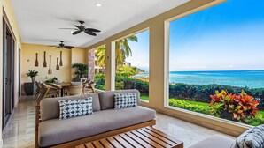 A modern living room with a sofa, coffee table, and dining area, overlooking a scenic ocean view. - Cozy Beachfront Apartment With Stunning Ocean Views and Resort Amenities (Puerto Vallarta)