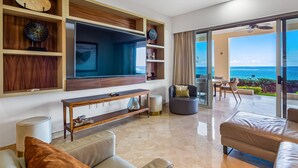 A modern living room with a TV, shelves, and a view of the ocean. - Cozy Beachfront Apartment With Stunning Ocean Views and Resort Amenities (Puerto Vallarta)