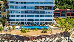 Ein mehrstöckiges Hotel mit Pool, umgeben von Felsen und Palmen.