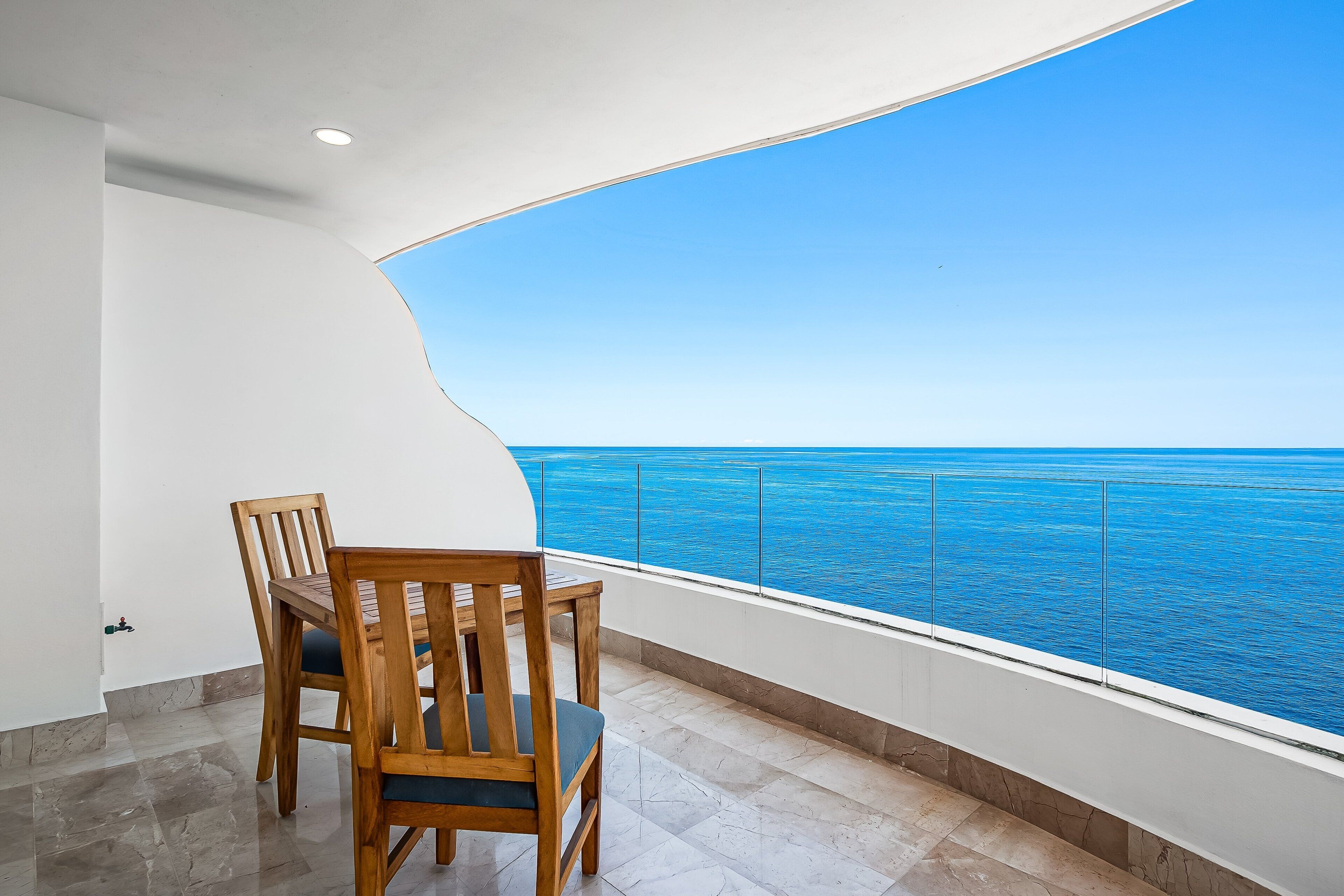 Un balcón con vista al océano, una mesa de madera y sillas.