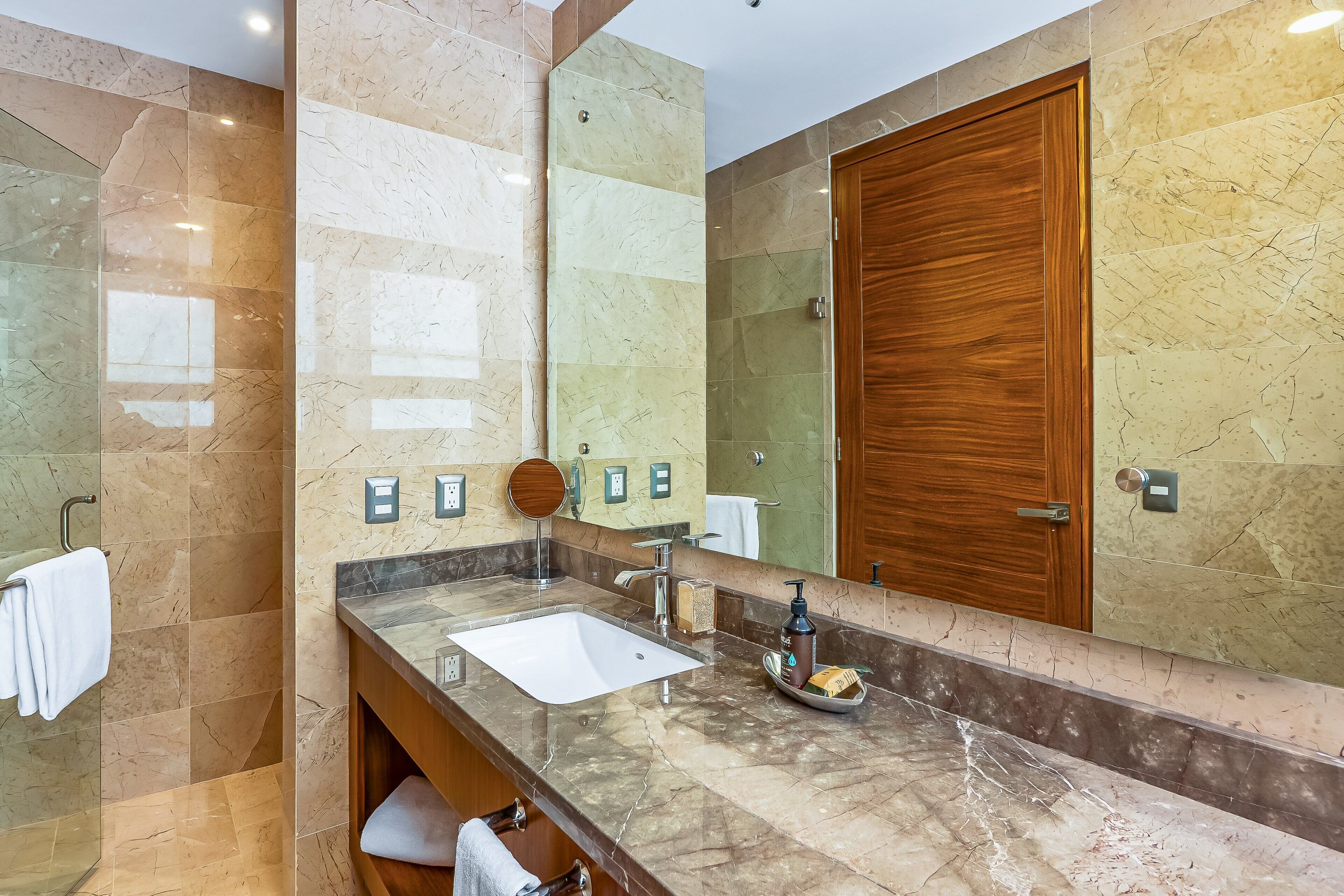 Un bagno con un lavabo in marmo, una porta in legno e uno specchio grande.