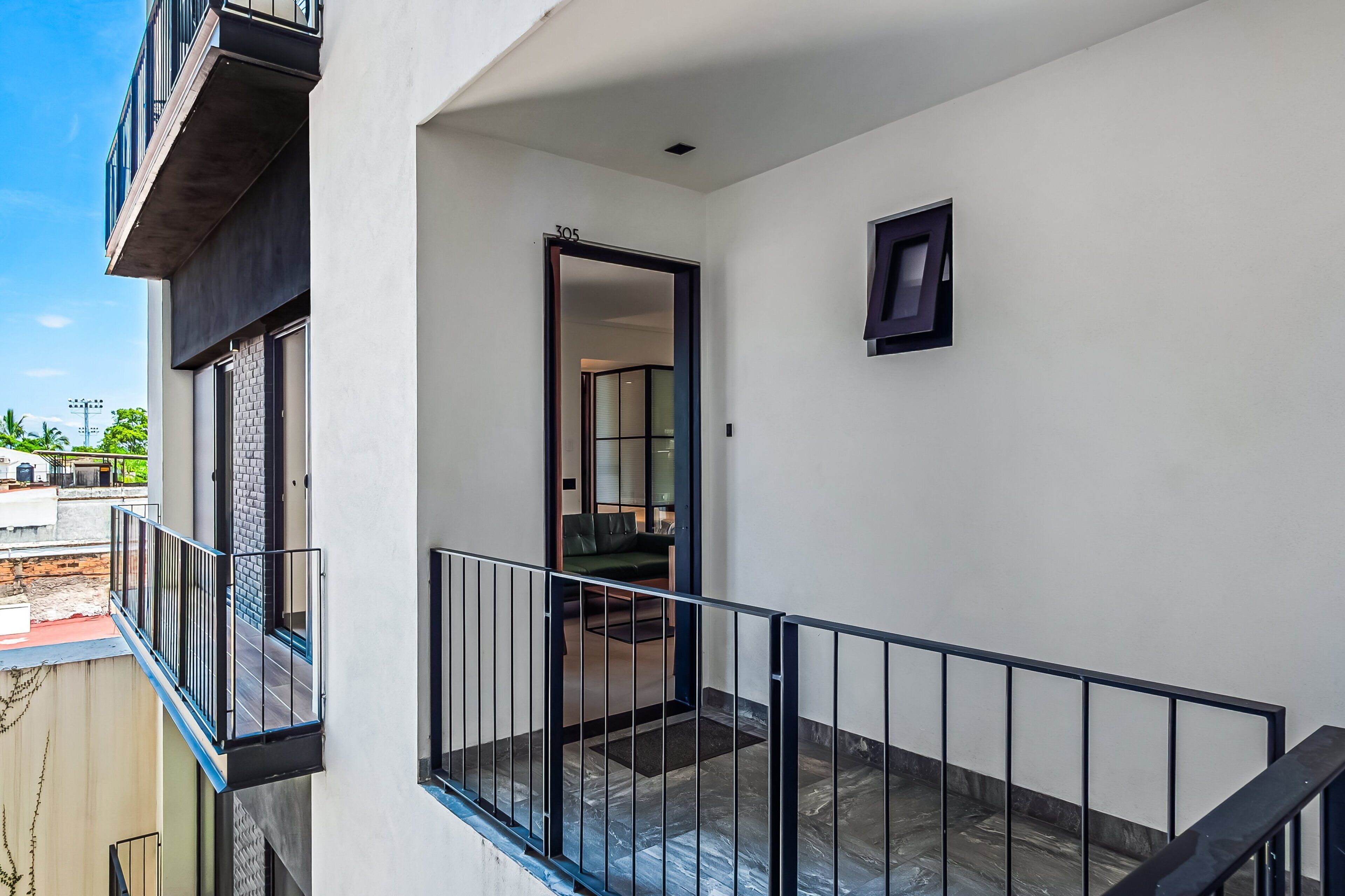 Een balkon met een zwarte reling, een deur die naar een binnenruimte leidt, en een klein raam in de muur.