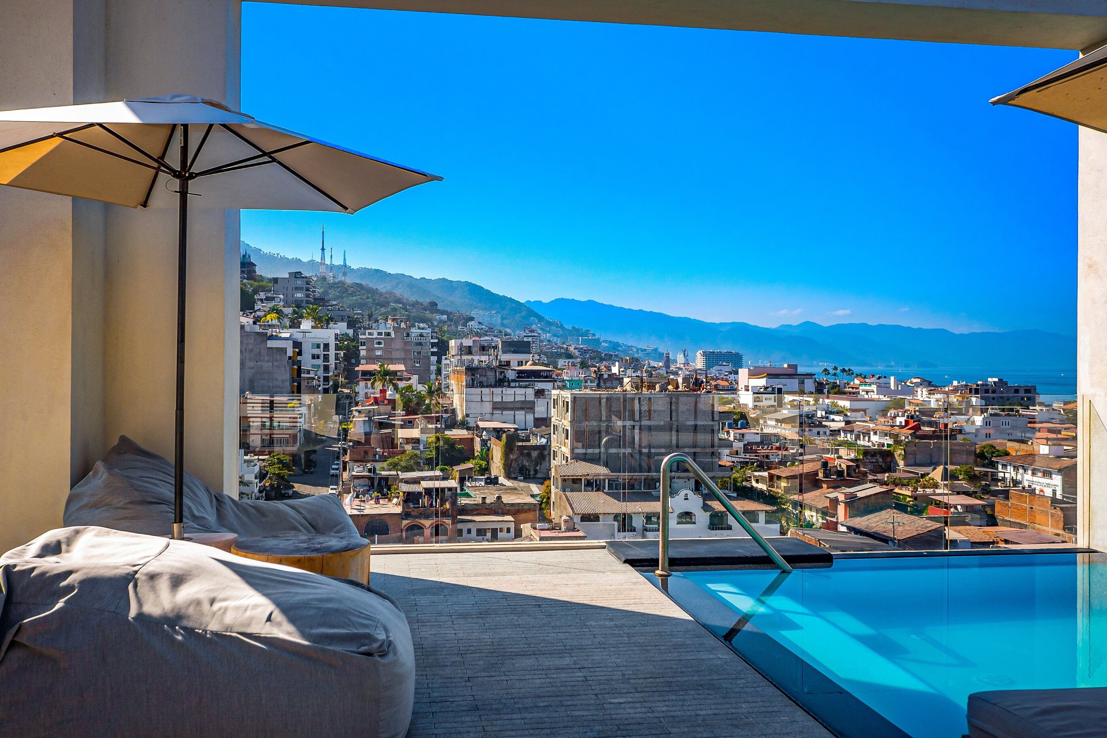 Un balcon avec une piscine, une vue sur la ville et un grand parasol.