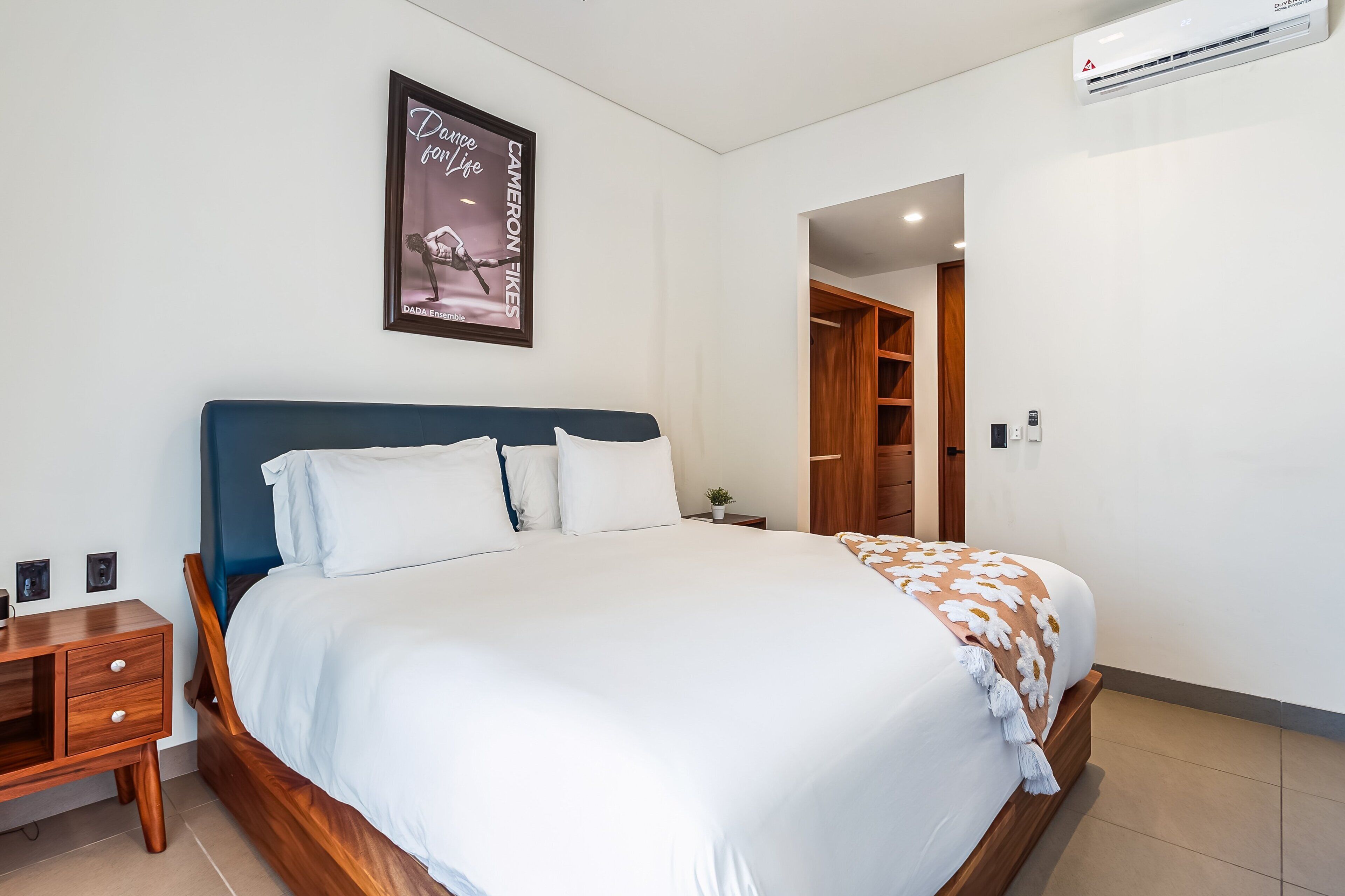 A neatly arranged bedroom with a bed, bedside table, and a poster on the wall.