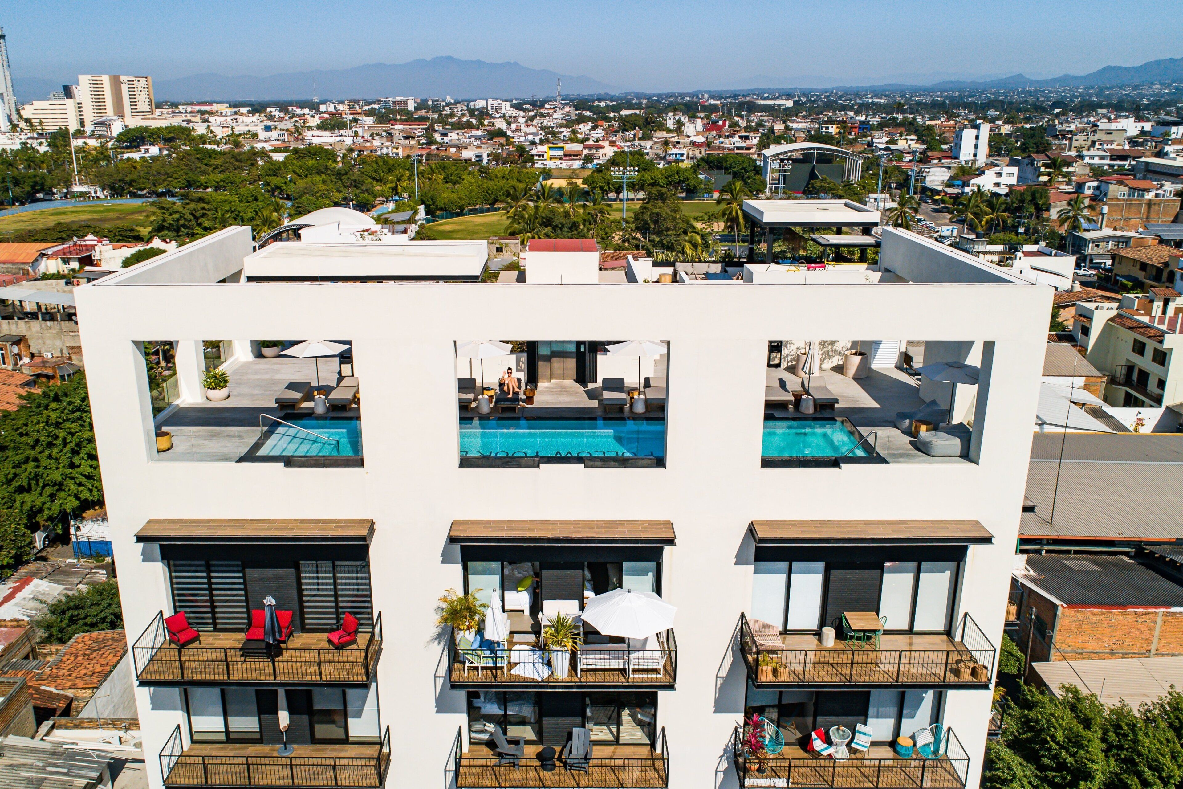 A modern building with multiple balconies, each with a pool and outdoor seating.