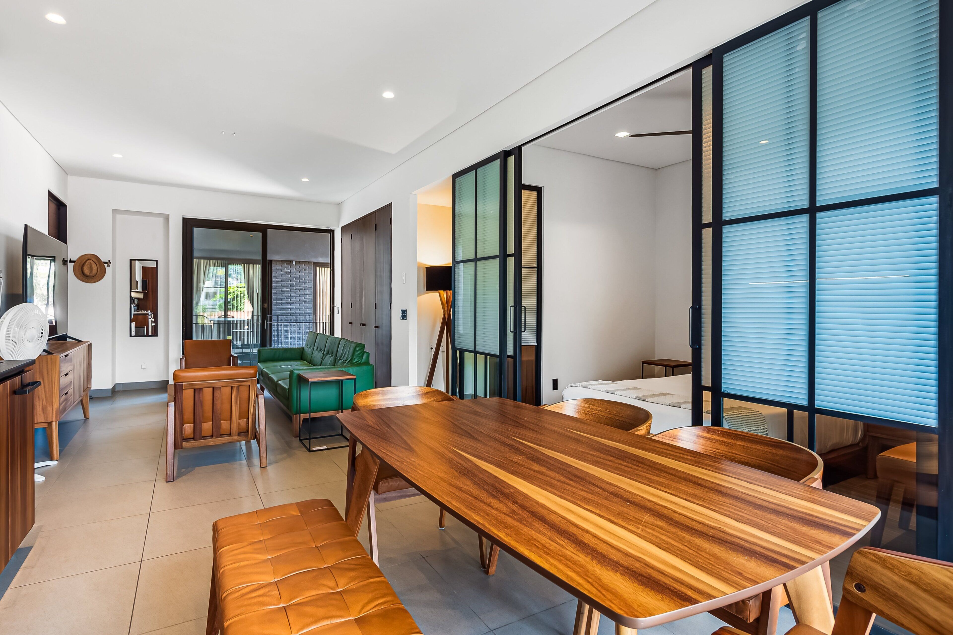 Una sala de estar moderna con una mesa de comedor de madera, un sofá verde y un amplio ventanal con persianas.