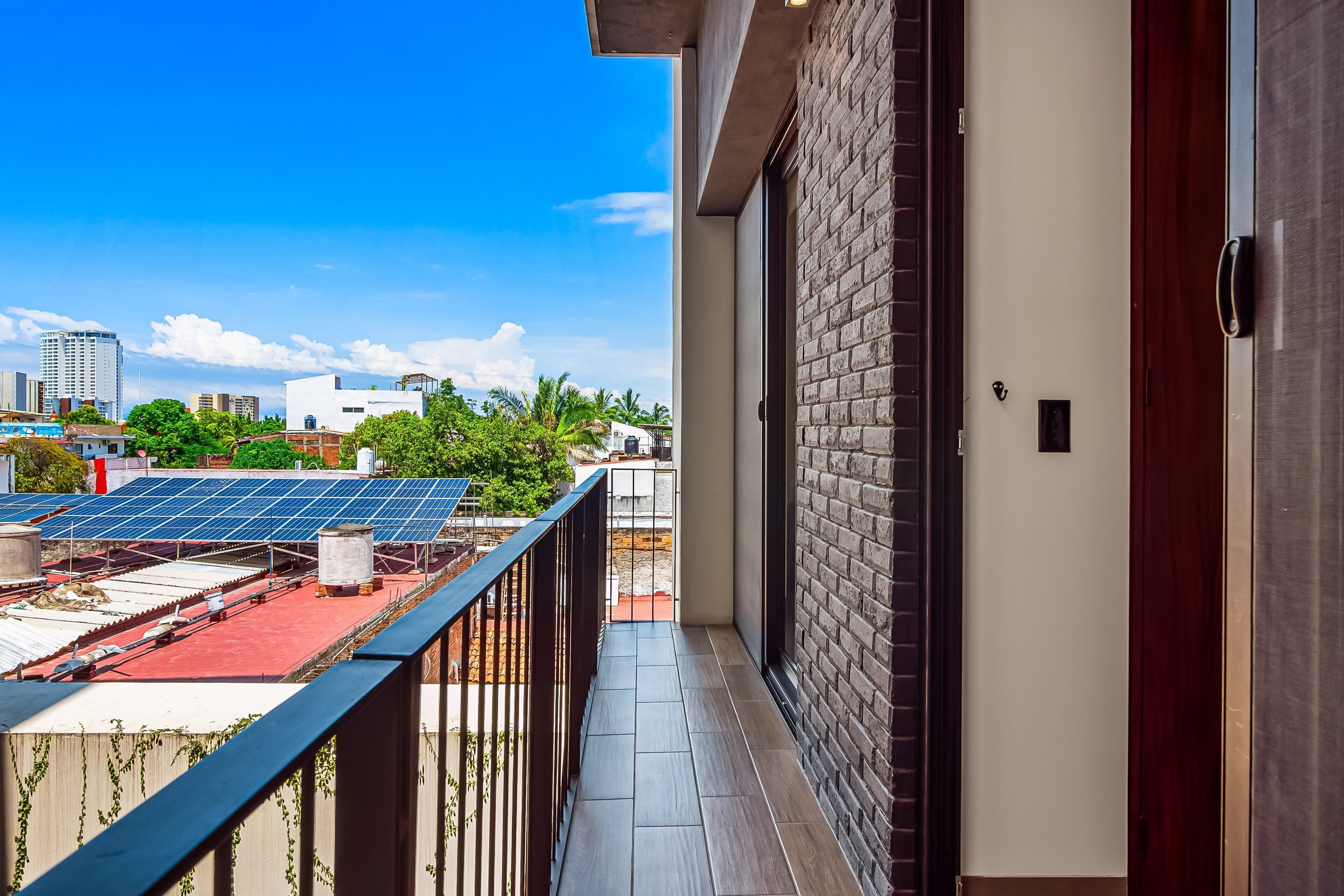 Un balcón con vista a paneles solares, un muro de ladrillo y una puerta.