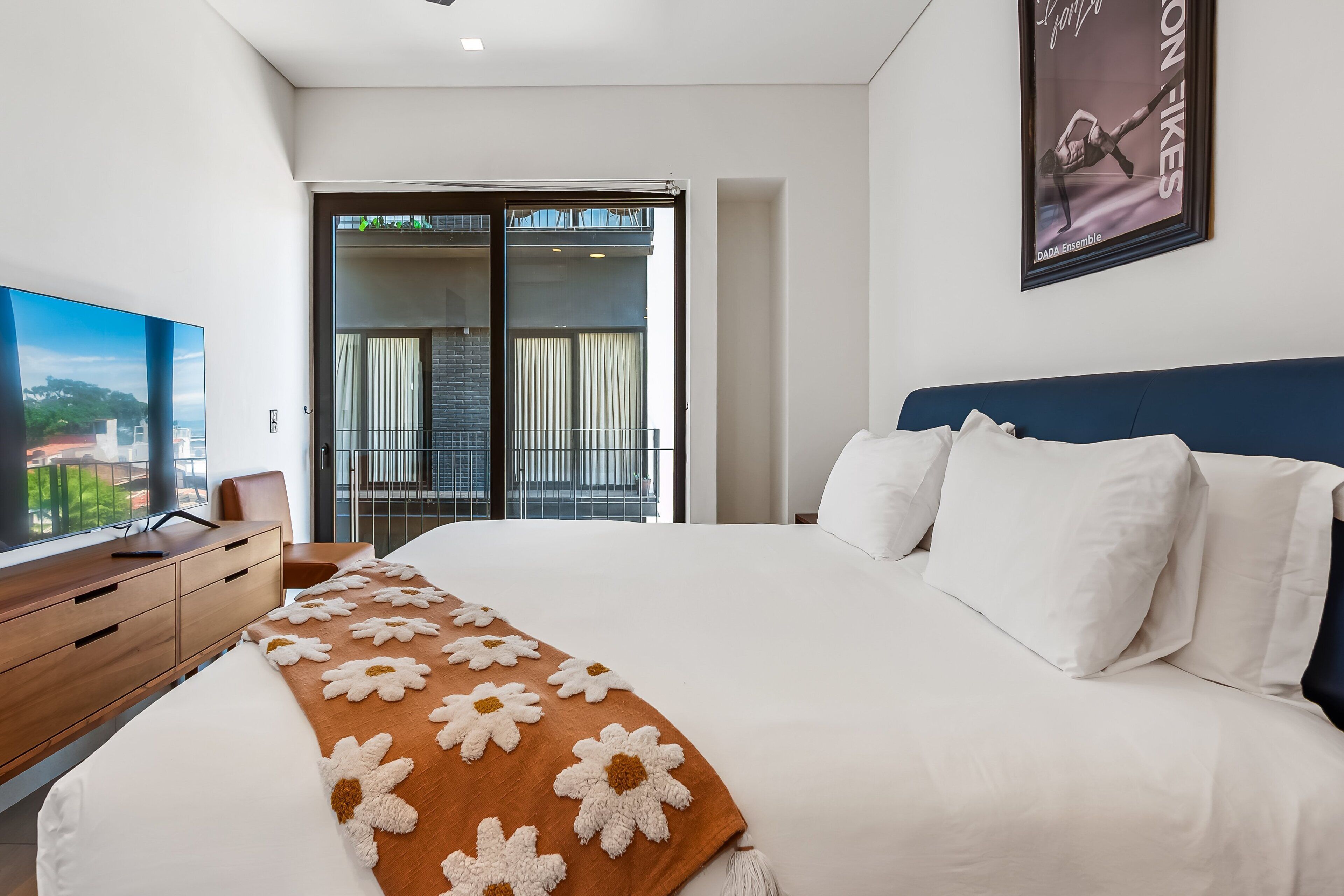 Una habitación de hotel moderna con una cama grande, televisor, escritorio y balcón con cortinas.