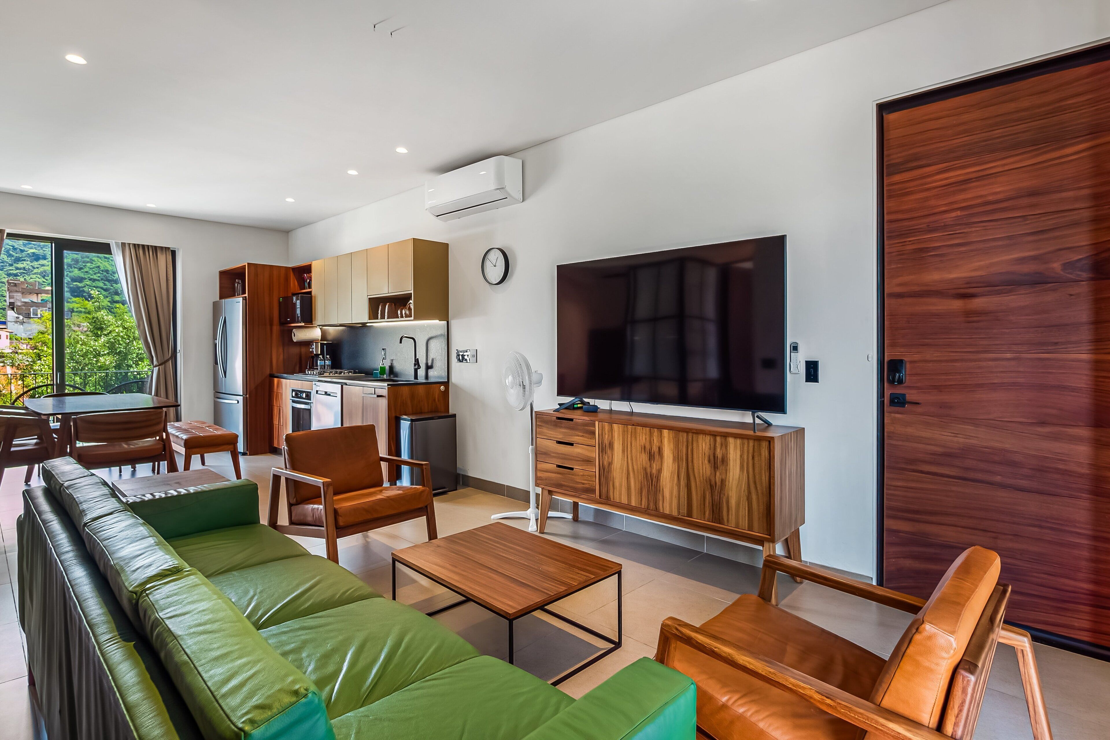 Ein modernes Wohnzimmer mit einer Couch, Sesseln, einem Couchtisch, einem Fernseher und einer Küchenzeile.