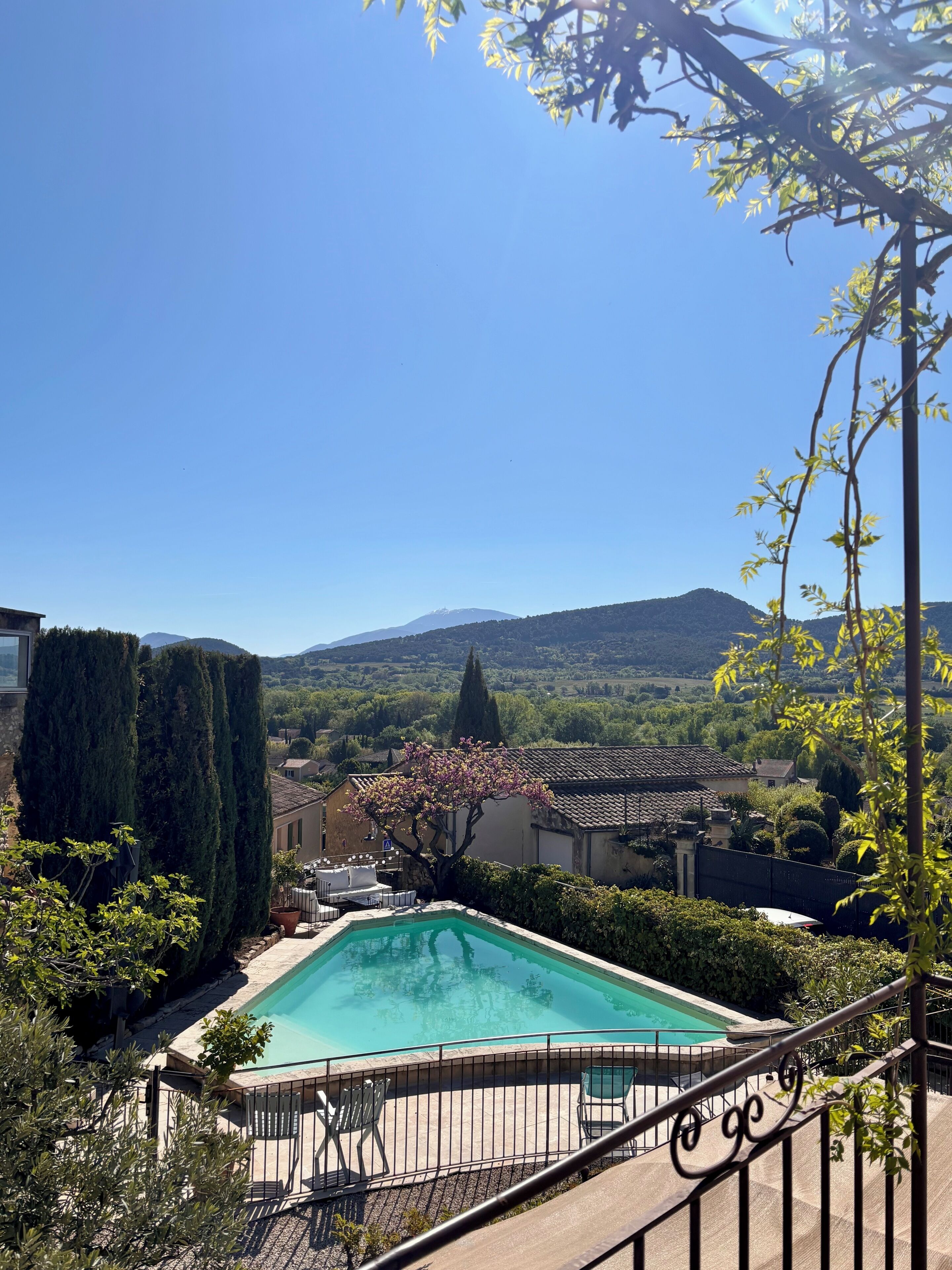 A pool with a view of mountains, a cypress tree, and a traditional building.