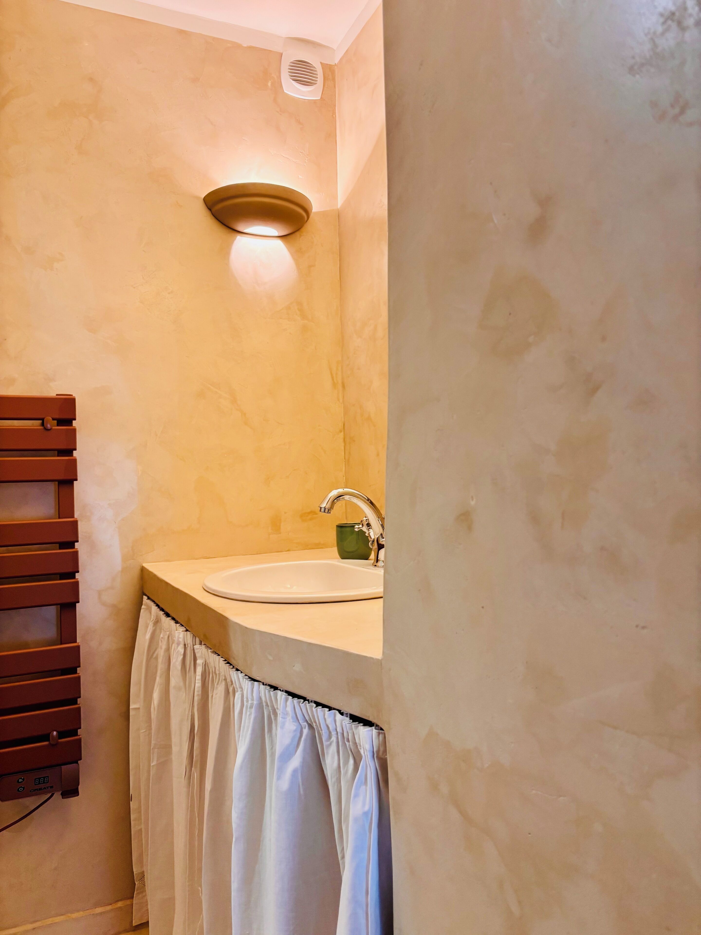 A bathroom with a sink, a towel rack, and a wall-mounted light fixture.