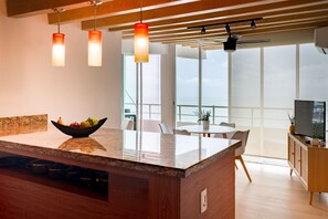 A modern kitchen with a central island, a bowl of fruit, and a dining area with a view. - Modern & Bright Condo With Ocean Views & Pool - Walk to the Beach (Puerto Vallarta)