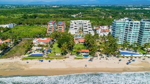 A coastal resort with beachfront villas, a pool area, and a beach with umbrellas. - Stylish Condo With Covered Balcony, Pool & Pool Tables (Nuevo Nayarit)