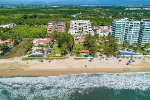 Un complejo turístico frente al mar con villas privadas en la playa, una zona de piscina y una playa con sombrillas.