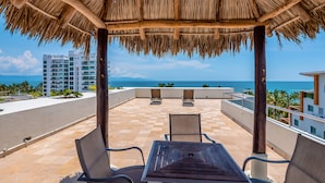 A covered outdoor seating area with a view of the ocean and buildings in the background. - Stylish Condo With Covered Balcony, Pool & Pool Tables (Nuevo Nayarit)