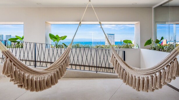 A hammock suspended from the ceiling in a spacious balcony with a city view. - Resort Condo With Balcony, Scenic View, Rooftop Pool, & Well-equipped Kitchen (Puerto Vallarta)