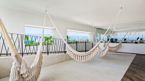 A spacious room with large windows, a hammock, and a balcony with a railing. - Resort Condo With Balcony, Scenic View, Rooftop Pool, & Well-equipped Kitchen (Puerto Vallarta)