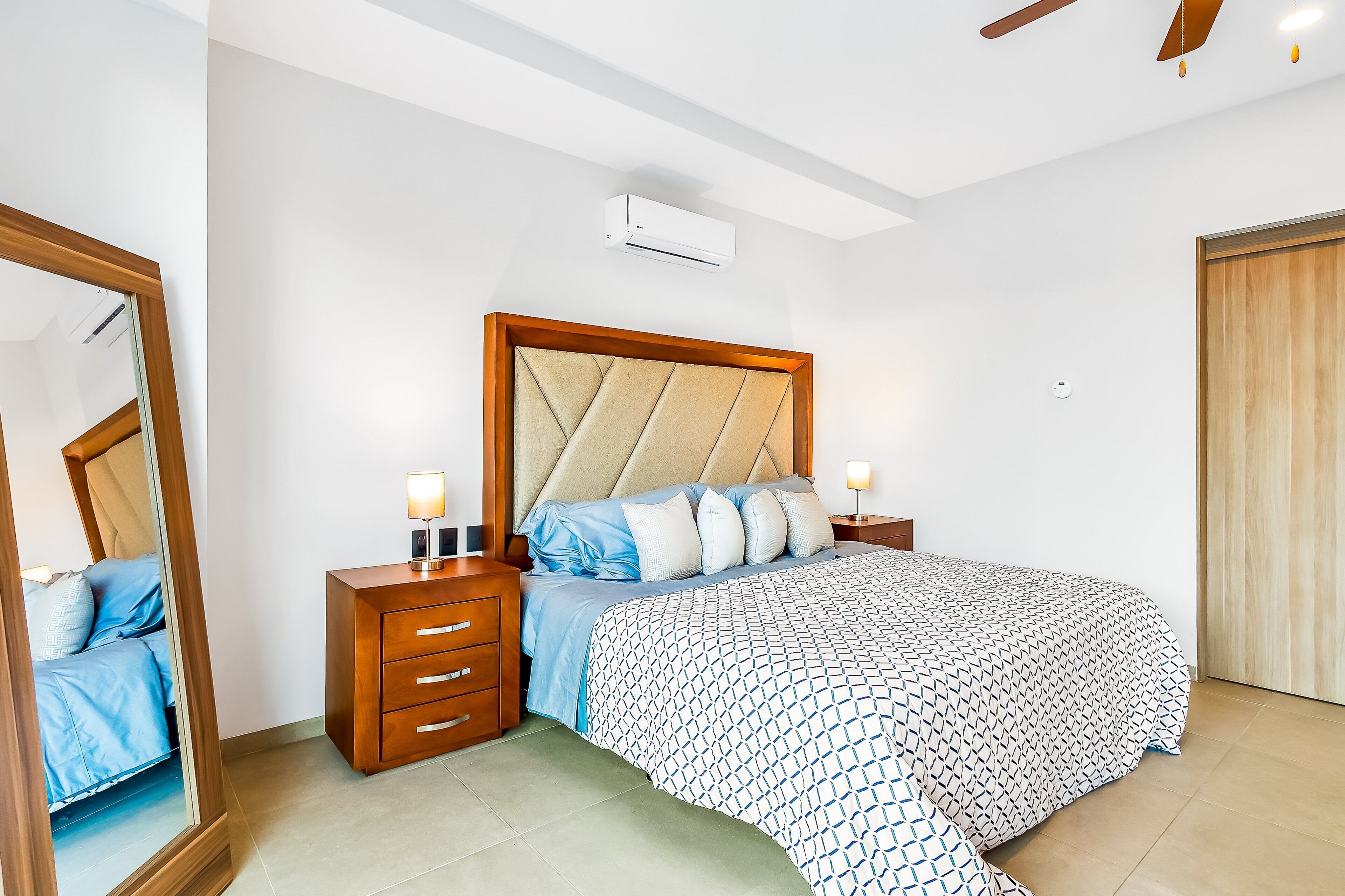 A bedroom with a bed, nightstands, a mirror, and a ceiling fan.