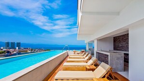 A poolside area with lounge chairs and a view of the city skyline. - Resort Condo With Balcony, Scenic View, Rooftop Pool, & Well-equipped Kitchen (Puerto Vallarta)