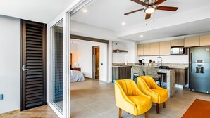 A modern kitchen with a built-in island, a dining area with yellow chairs, and a sliding glass door leading to a living space. - Resort Condo With Balcony, Scenic View, Rooftop Pool, & Well-equipped Kitchen (Puerto Vallarta)